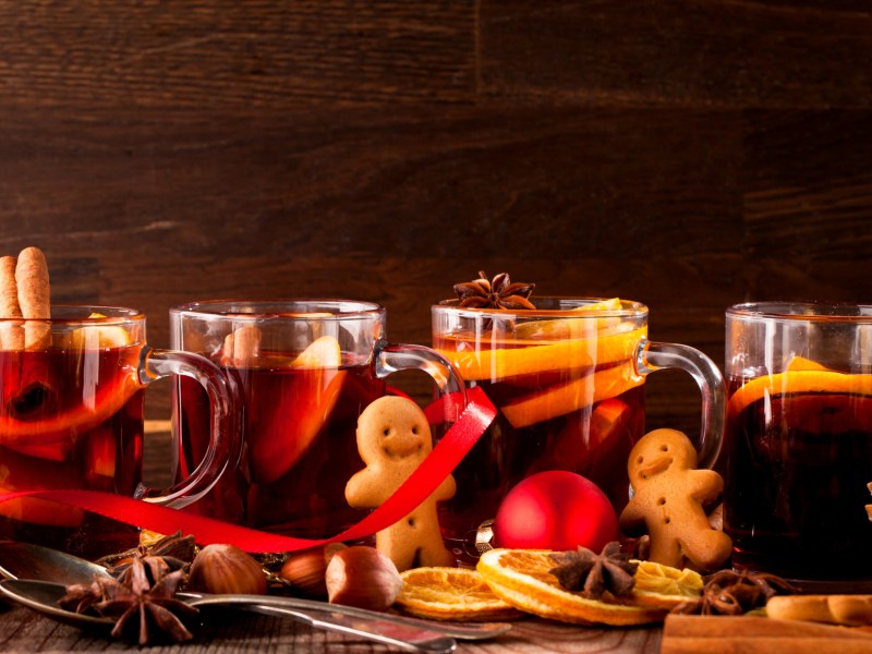 Auf einem weihnachtlich geschmückten Tisch stehen Gläser mit Glühwein, Punsch und Lebkuchenmänner.