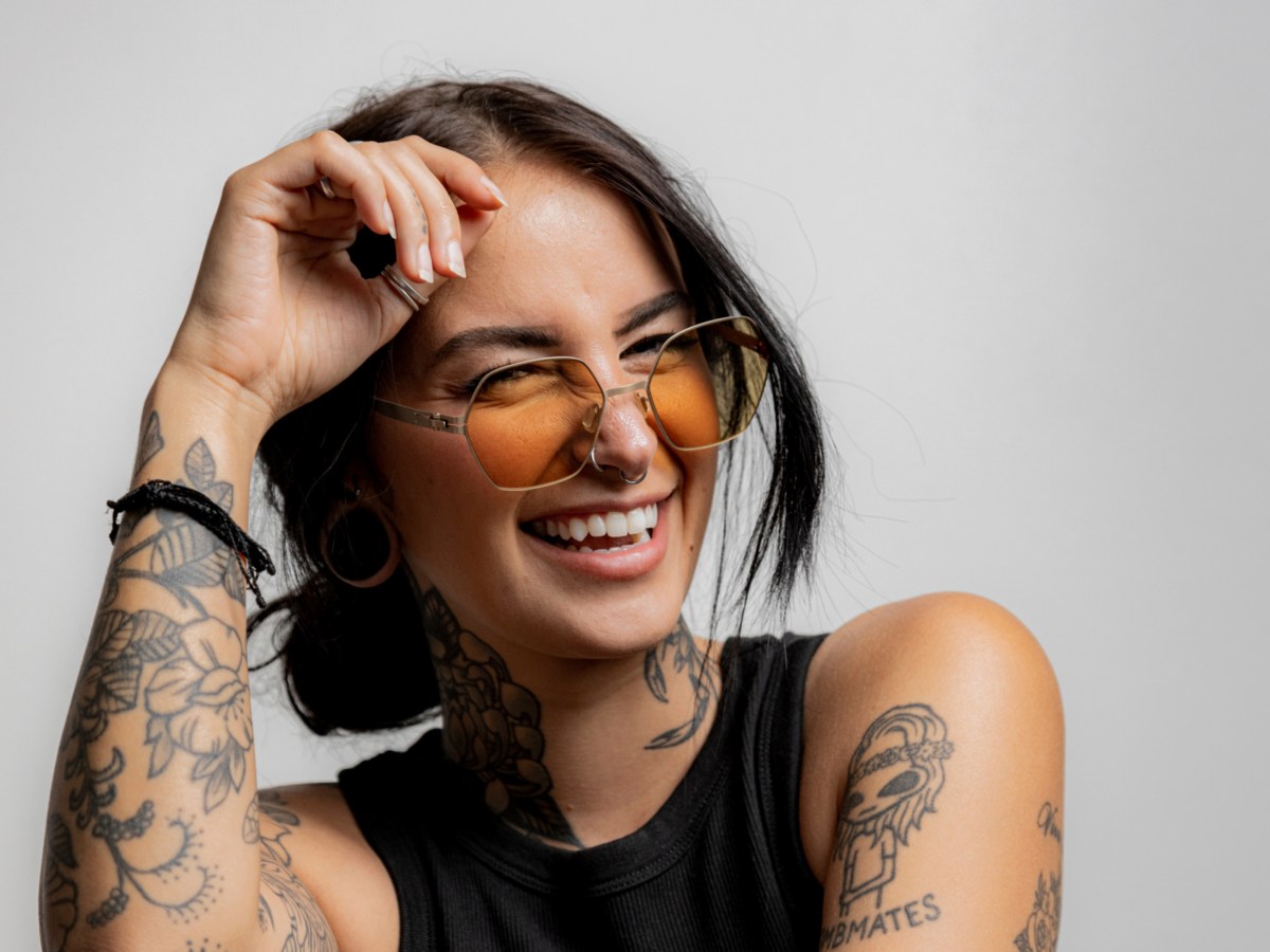 Frau mit Sonnenbrille und Tattoos, die in die Kamera lacht