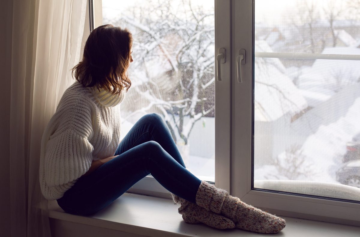 Frau sitzt vor Fenster, dahinter Winterlandschaft