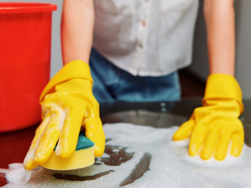 Frau putzt mit Handschuhen und Schwamm eine Oberfläche