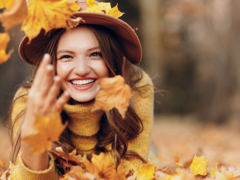 Frau liegt in gelbem Herbstlaub und lächelt.