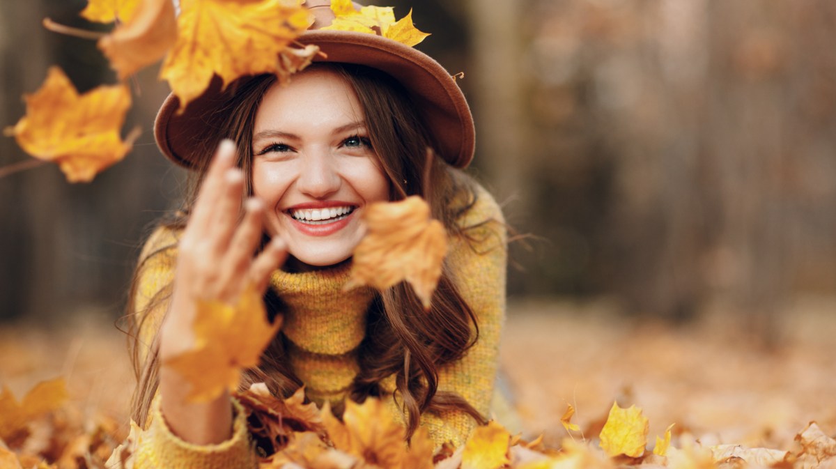 Frau liegt in gelbem Herbstlaub und lächelt.