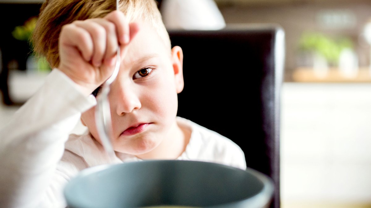 Nahaufnahme eines Jungen, der am Tisch sitzt und seine Suppe vor ihm nicht essen möchte.