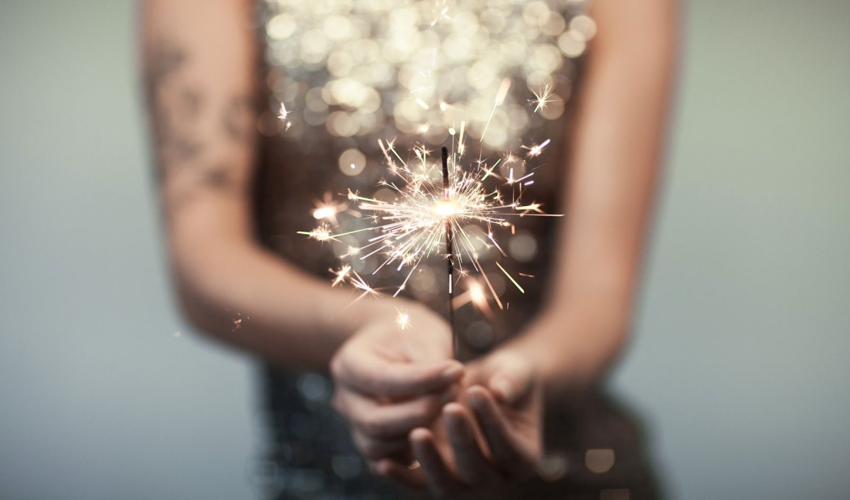 Frau in einem Glitzerkleid hält eine Wunderkerze in der Hand