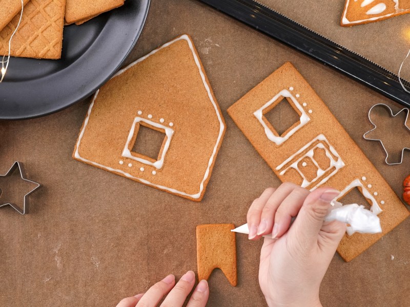 Eine Hand dekoriert Lebkuchen für ein Lebkuchenhaus.