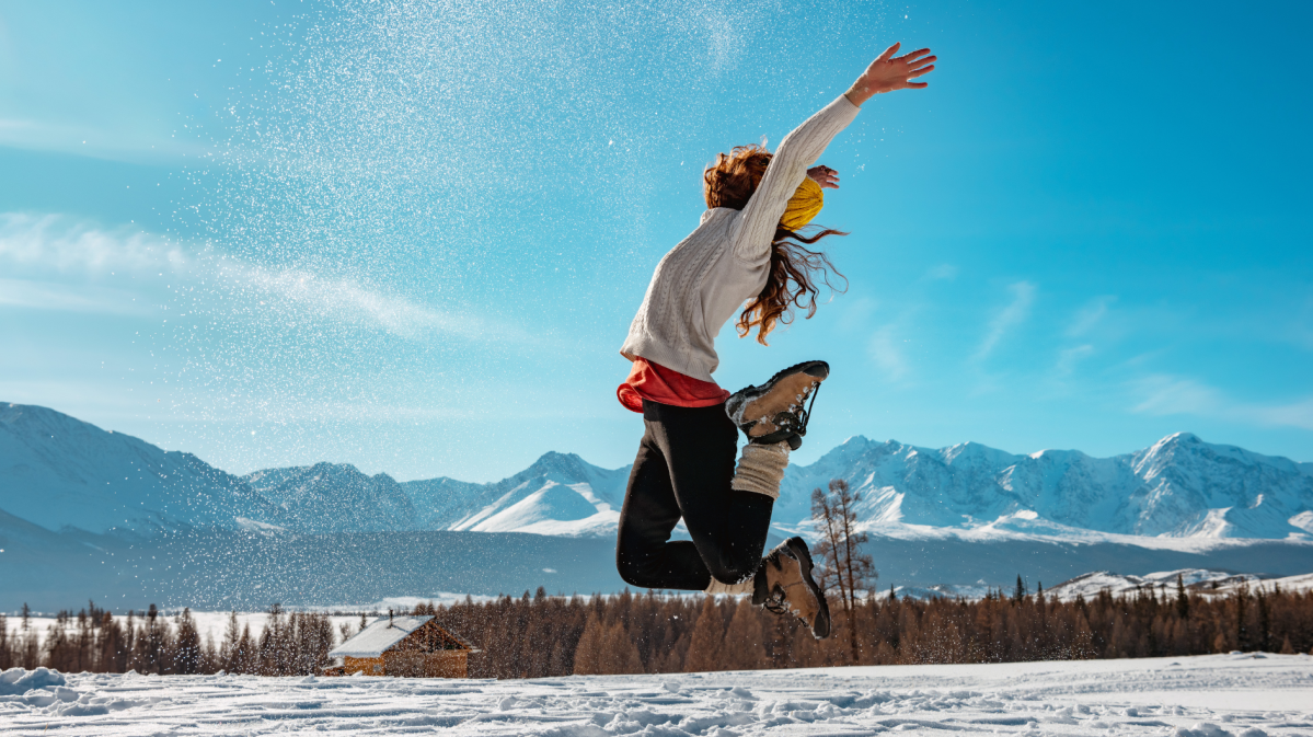 Frau die im Schnee in die Luft springt und die Arme hochreißt