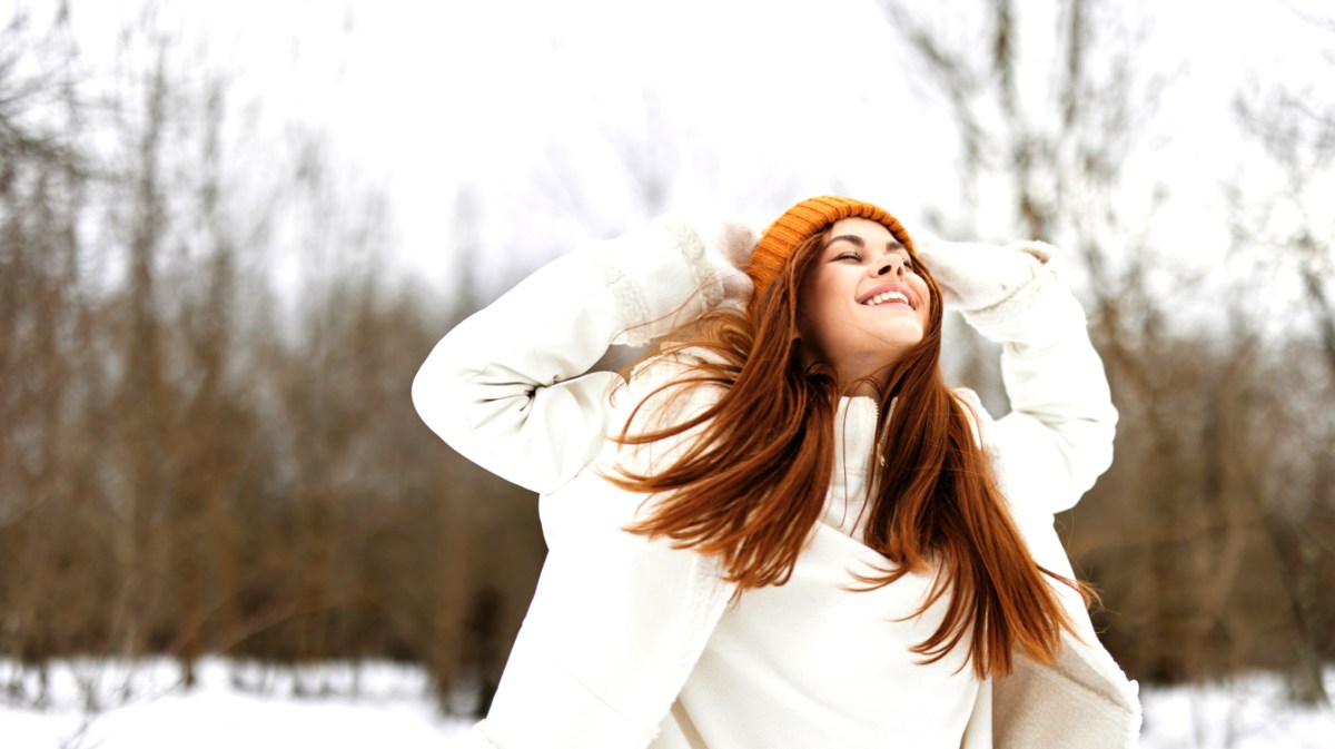 Frau im Schnee mit roten Haaren die lacht und sich an den Kopf packt