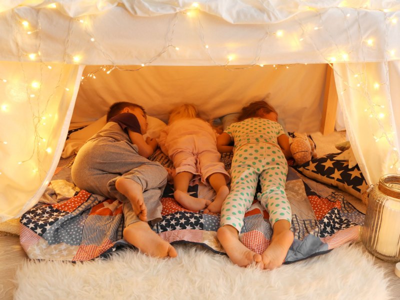 Drei Kinder unterschiedlichen Alters schlafen in einer Höhle im Zimmer.