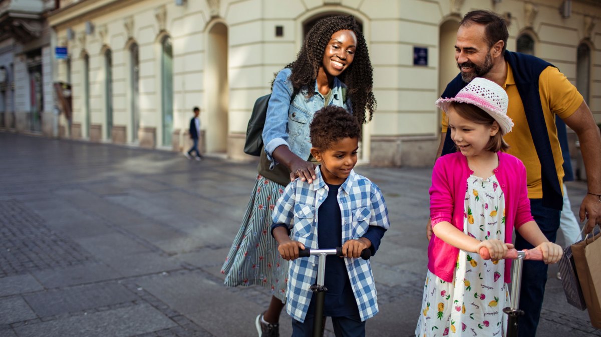 Stieffamilie ist in der Stadt unterwegs. Die beiden Kinder fahren mit Rollern.