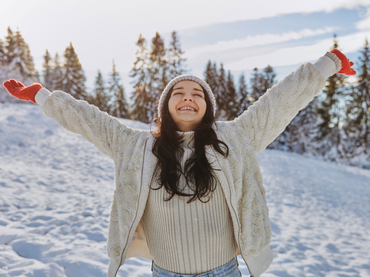 Frau in WInterbekleidung mit ausgestreckten Armen vor winterlicher Landschaft