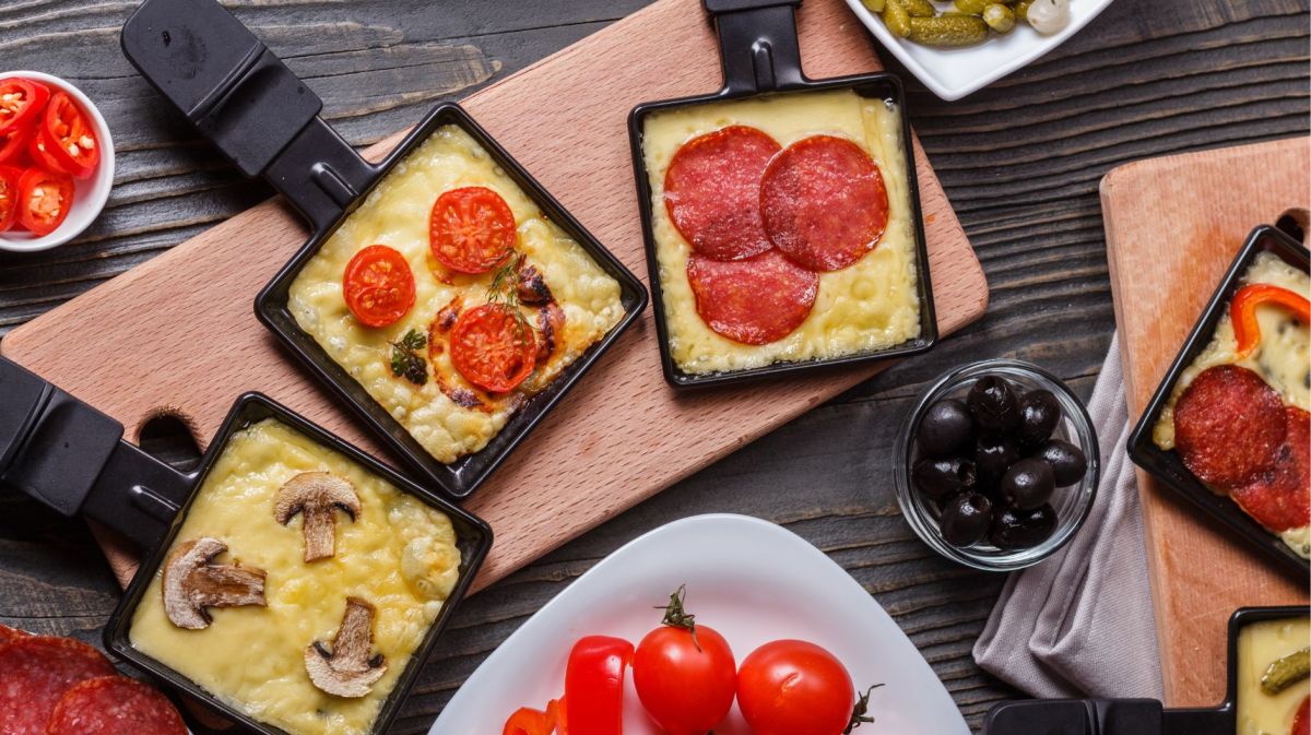 Raclette Pfännchen mit Käse und Zutaten gefüllt.