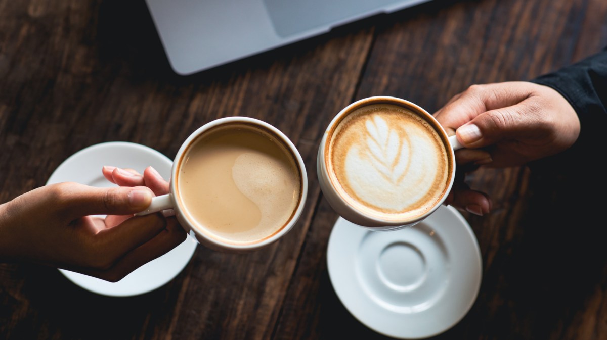 Zwei Frauen mit stoßen mit Kaffeetassen an.