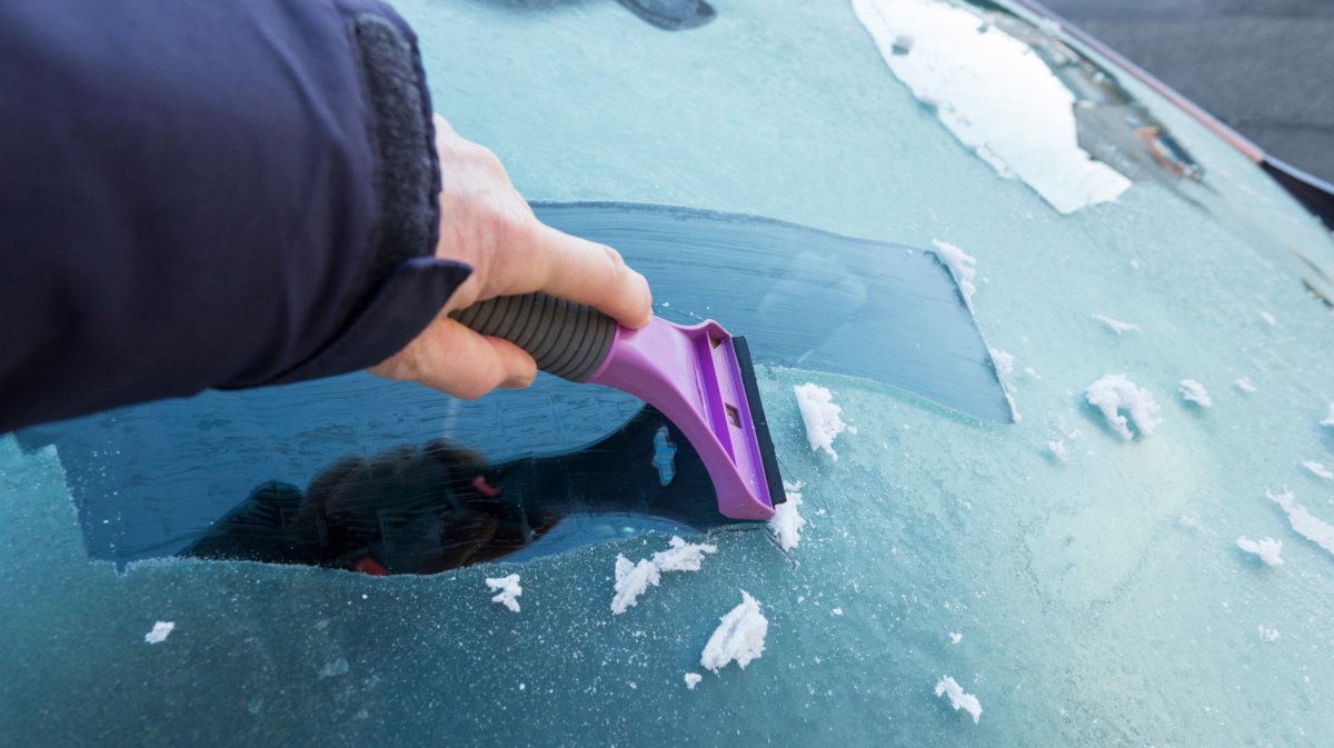 Person kratzt gefrorene Autoscheibe mit einem Eiskratzer frei