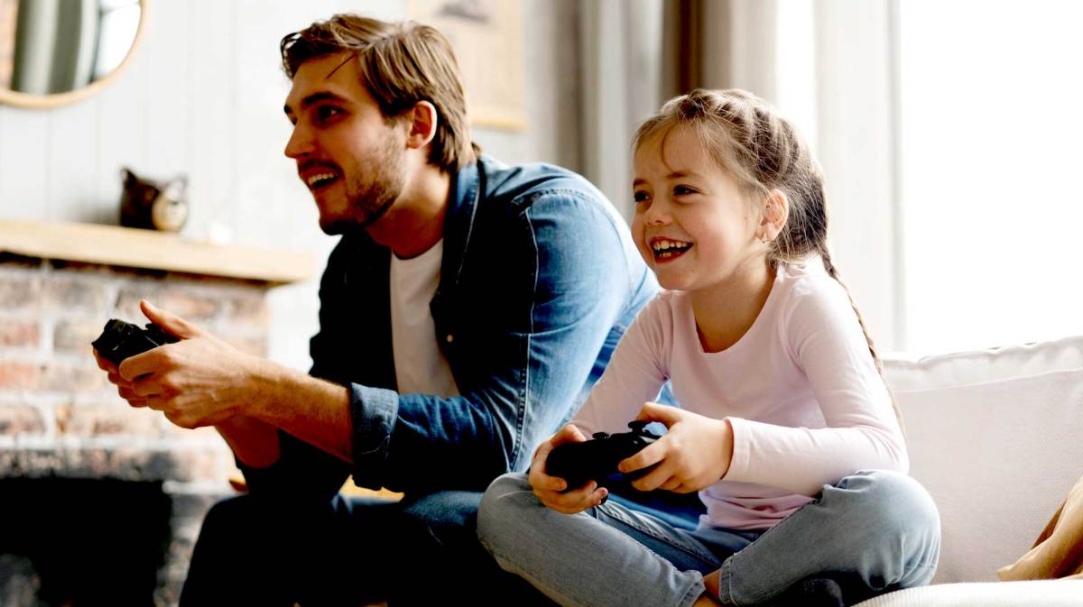 Vater und Tochter sitzen mit Controllern auf dem Sofa und freuen sich.