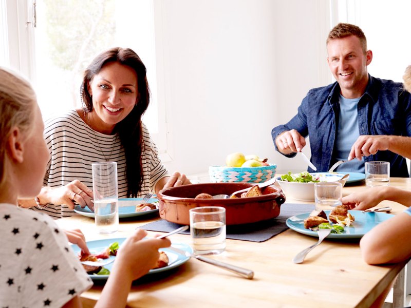 Mutter, Vater, Sohn und Tochter sitzen gemeinsam beim Essen am Tisch.