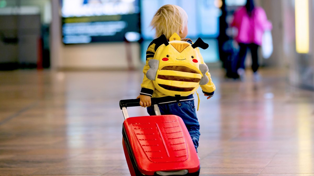 Kleines Kind, ca. vier Jahre, mit Rucksack und Rollkoffer am Flughafen.