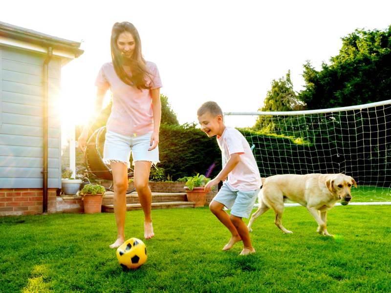 Mutter und Sohn spielen bei schönem Wetter Fußball im Garten.