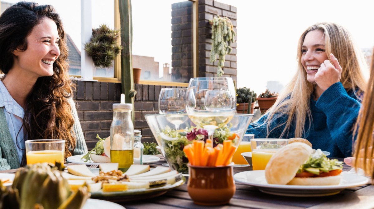 Frauen lachend am Tisch mit vielen gesunden Speisen & Getränken