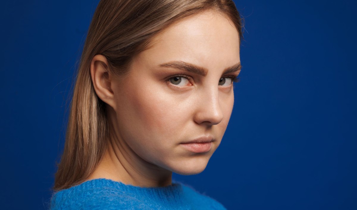 Blonde Frau schaut ernst in die kamera, dahinter blauer Hintergrund