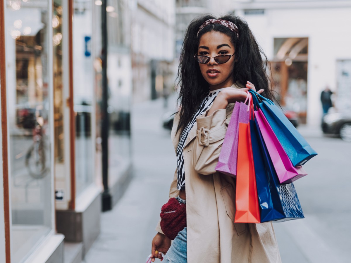 Junge Frau beim Shopping, hat mehrere Einkaufstaschen über Schulter geworfen.