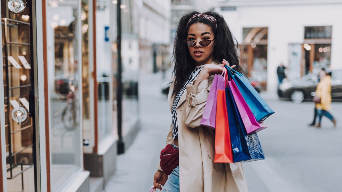 Junge Frau beim Shopping, hat mehrere Einkaufstaschen über Schulter geworfen.