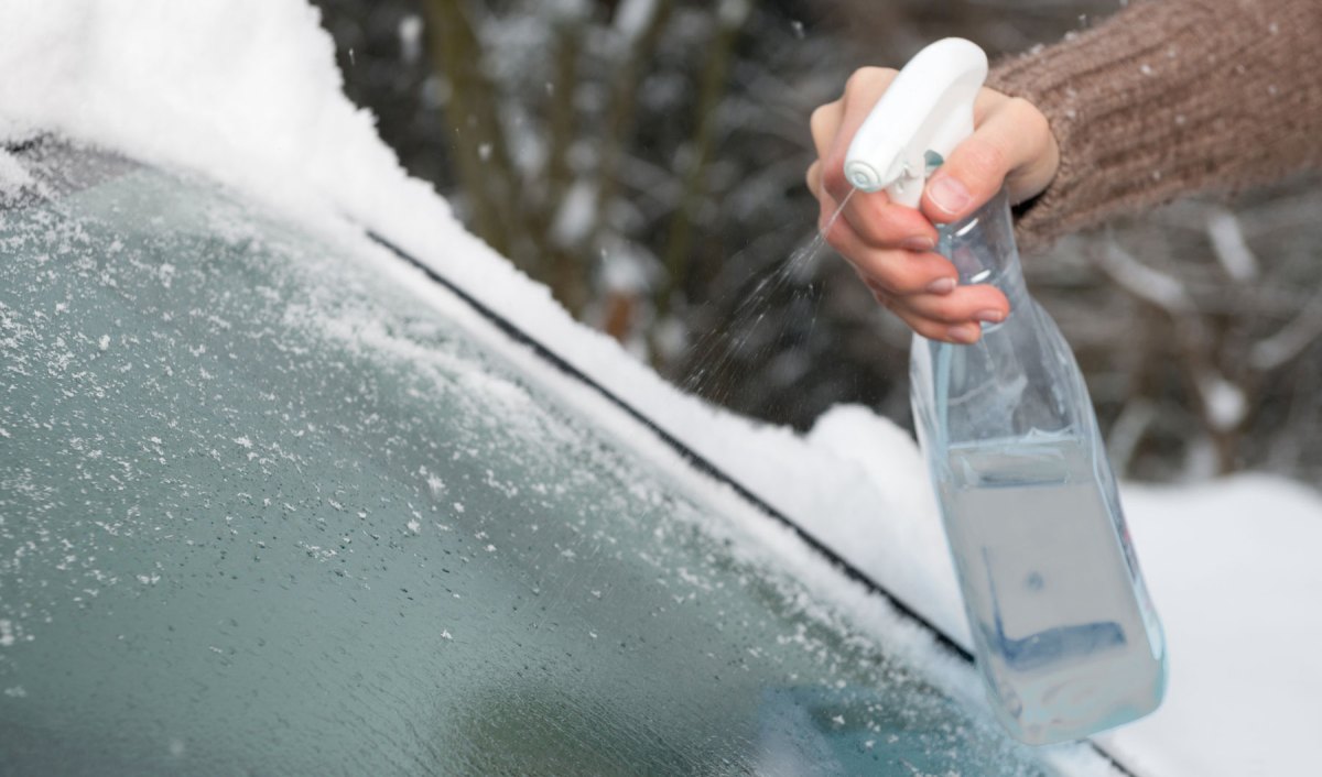 Person enteist die Scheibe mit Sprayflasche