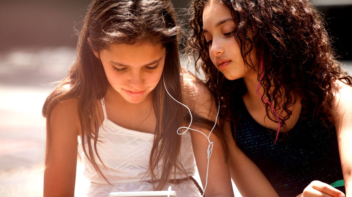 Zwei Mädchen sitzen am Tablet und hören Musik.