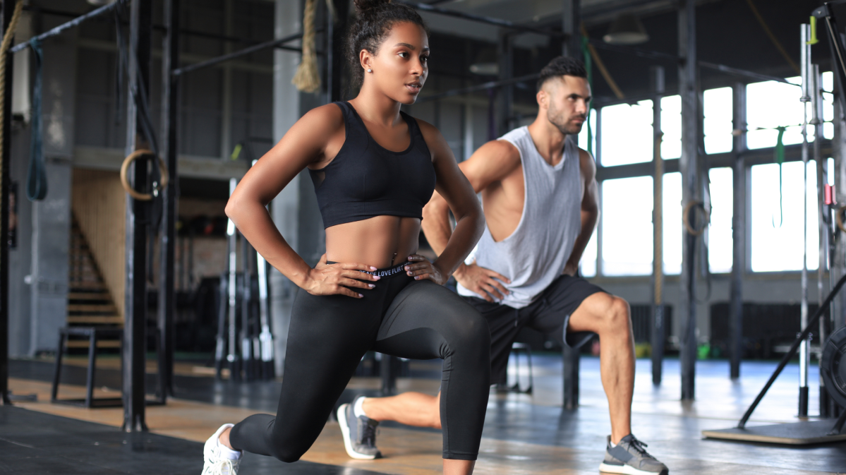 Frau und Mann im Fitnessstudio, die beide eine Kniebeuge machen und konzentriert nach vorne schauen