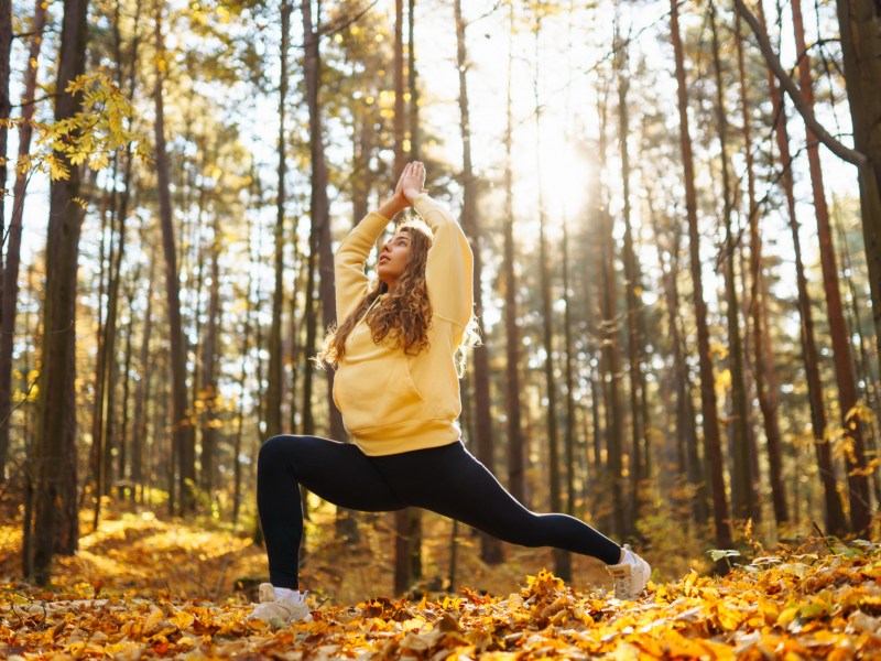 Frau im Wald die eine Yoga-Position macht und die Arme in die Luft hebt