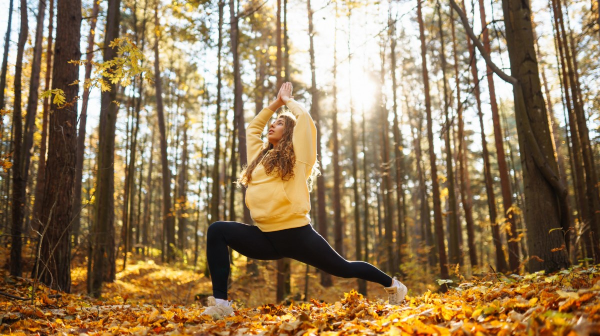 Frau im Wald die eine Yoga-Position macht und die Arme in die Luft hebt