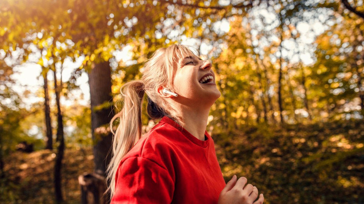 Frau im Wald, die lachend in Richtung Sonne schaut