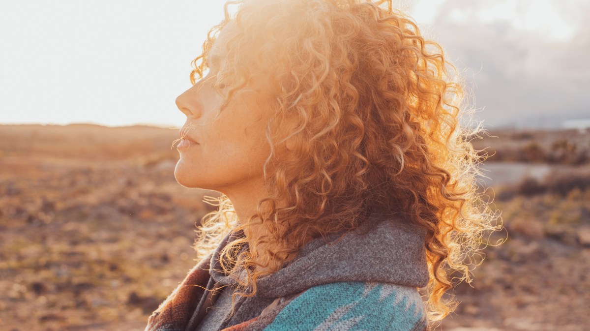 Frau in der Natur mit Locken, die genussvoll in die Sonne blickt