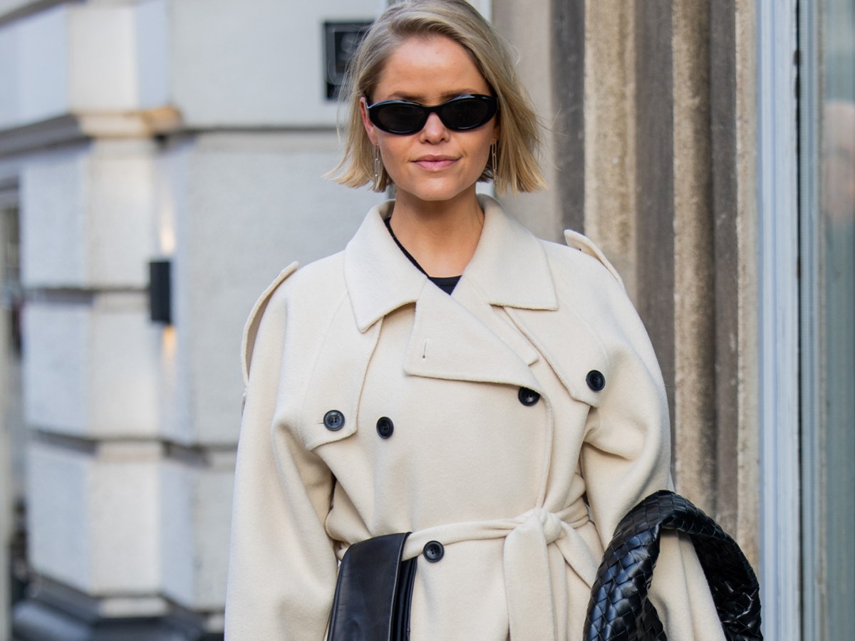 Cathrine Leth Damgaard wears beige trench coat, black bag, gloves, skirt, sunglasses outside The Garment during the Copenhagen Fashion Week AW24 on January 31, 2024 in Copenhagen