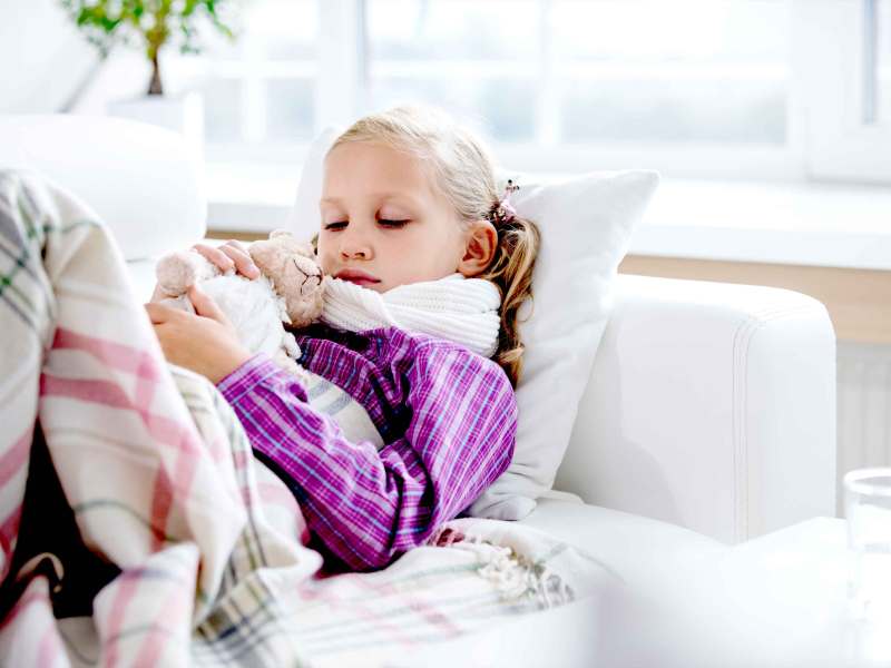 Mädchen, ca. 8 Jahre alt, liegt mit einem Schal um den Hals und zugedeckt auf dem Sofa.