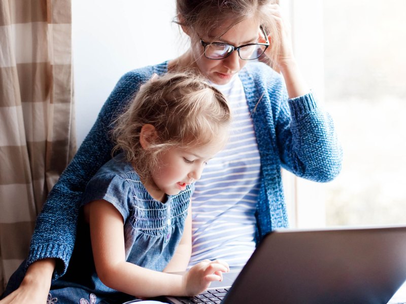 Berufstätige Mutter versucht, konzentriert von zu Hause aus zu arbeiten, während ihre Tochter auch zu Hause ist und sie am PC stört.