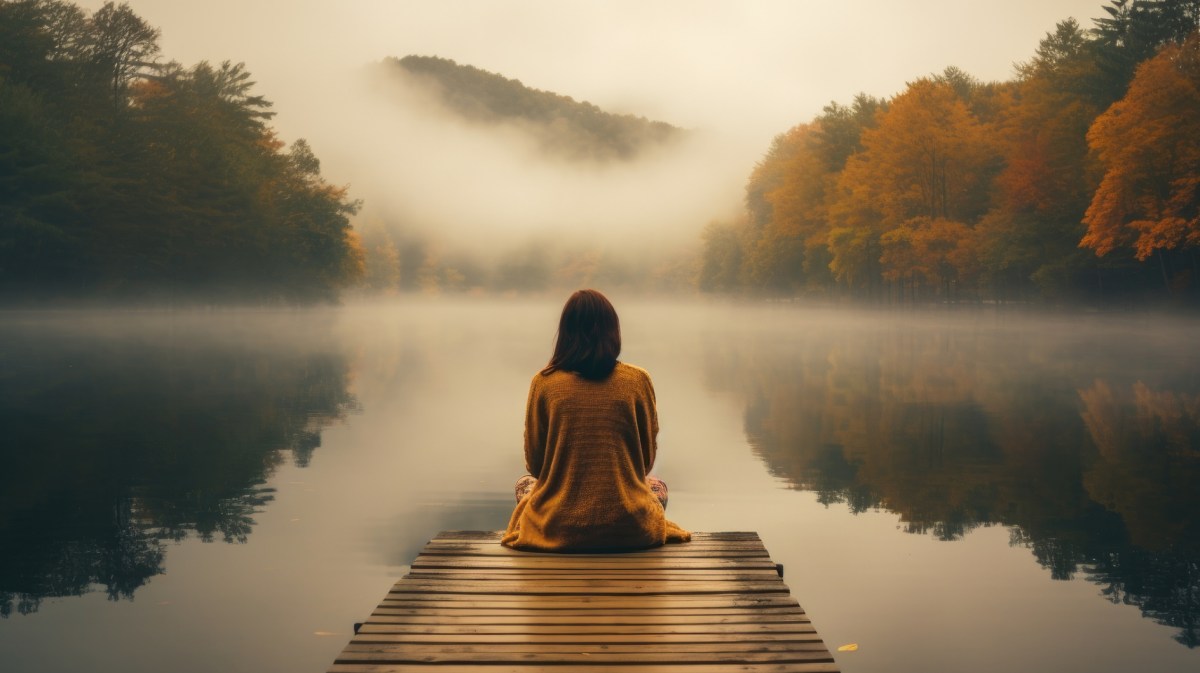 Frau auf einem Steg vor einem See im Herbst