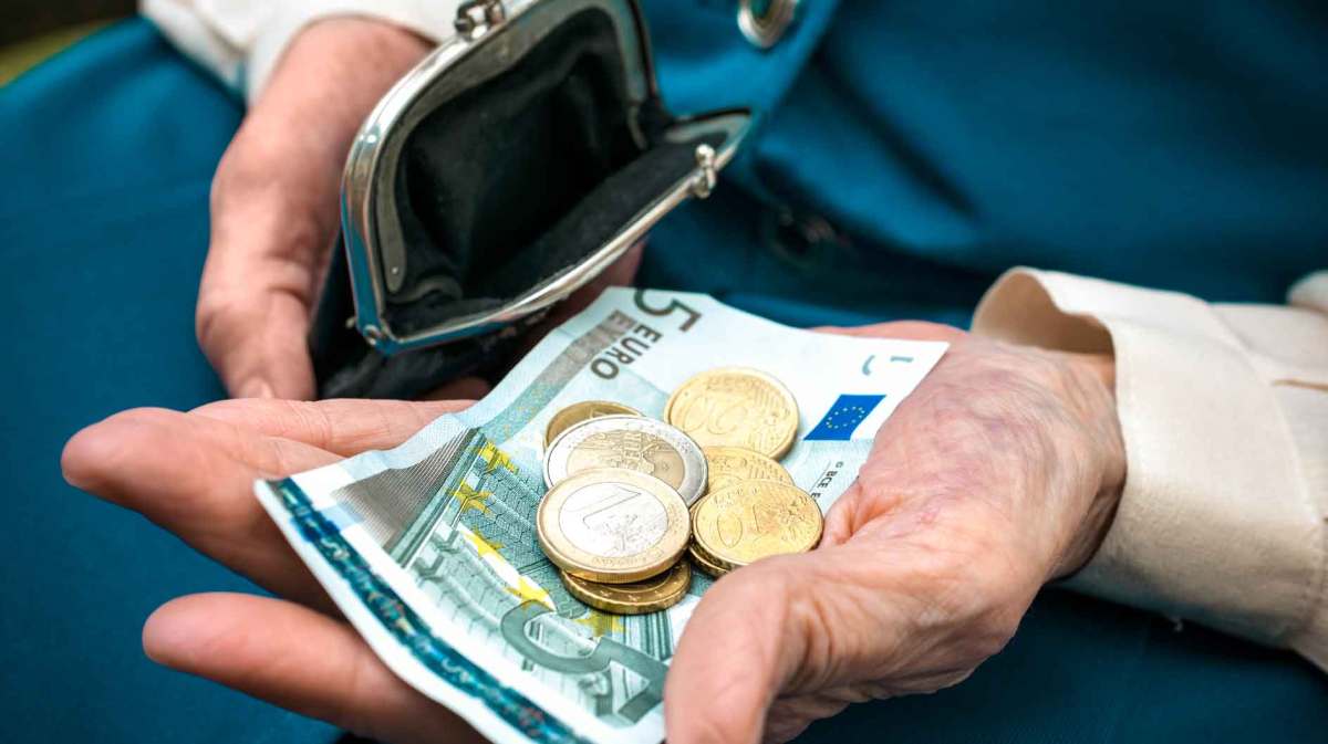 Ältere Frau hat Geld aus ihrer Geldbörse genommen und hält Scheine und Münzgeld in der Hand.