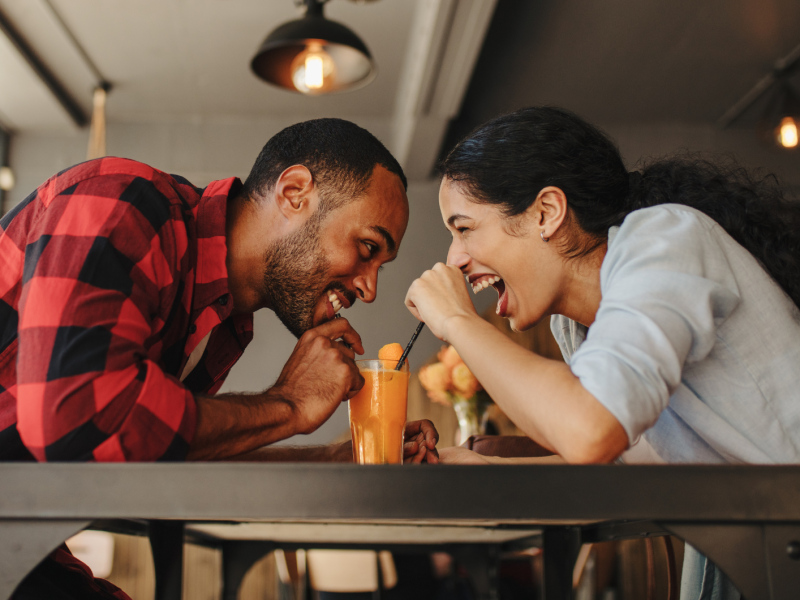 Frau und Mann in einem Café, die sich anlachen und dabei ein Getränk trinken.