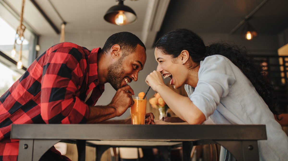 Frau und Mann in einem Café, die sich anlachen und dabei ein Getränk trinken.