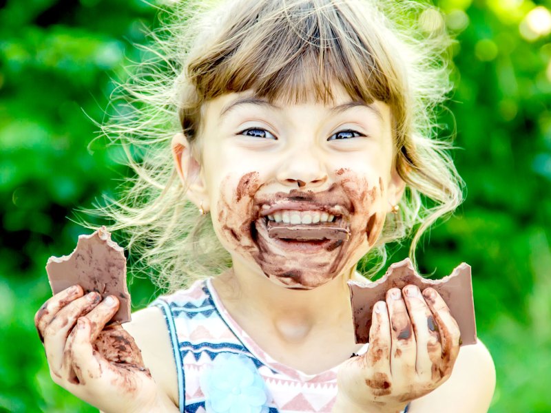Mädchen, ca. 8 Jahre, strahlt mit Schokolade verschmiertem Gesicht in die Kamera und hält in jeder Hand eine Tafel Schokolade.