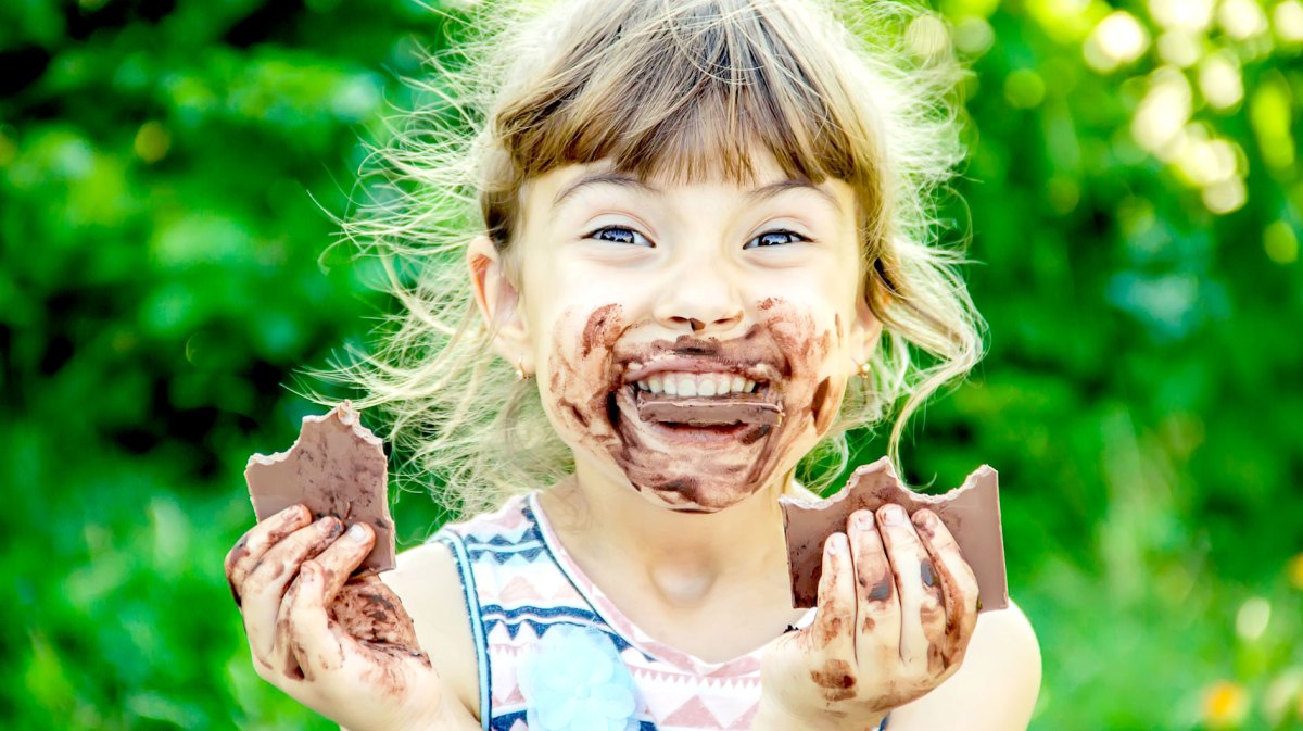 Mädchen, ca. 8 Jahre, strahlt mit Schokolade verschmiertem Gesicht in die Kamera und hält in jeder Hand eine Tafel Schokolade.