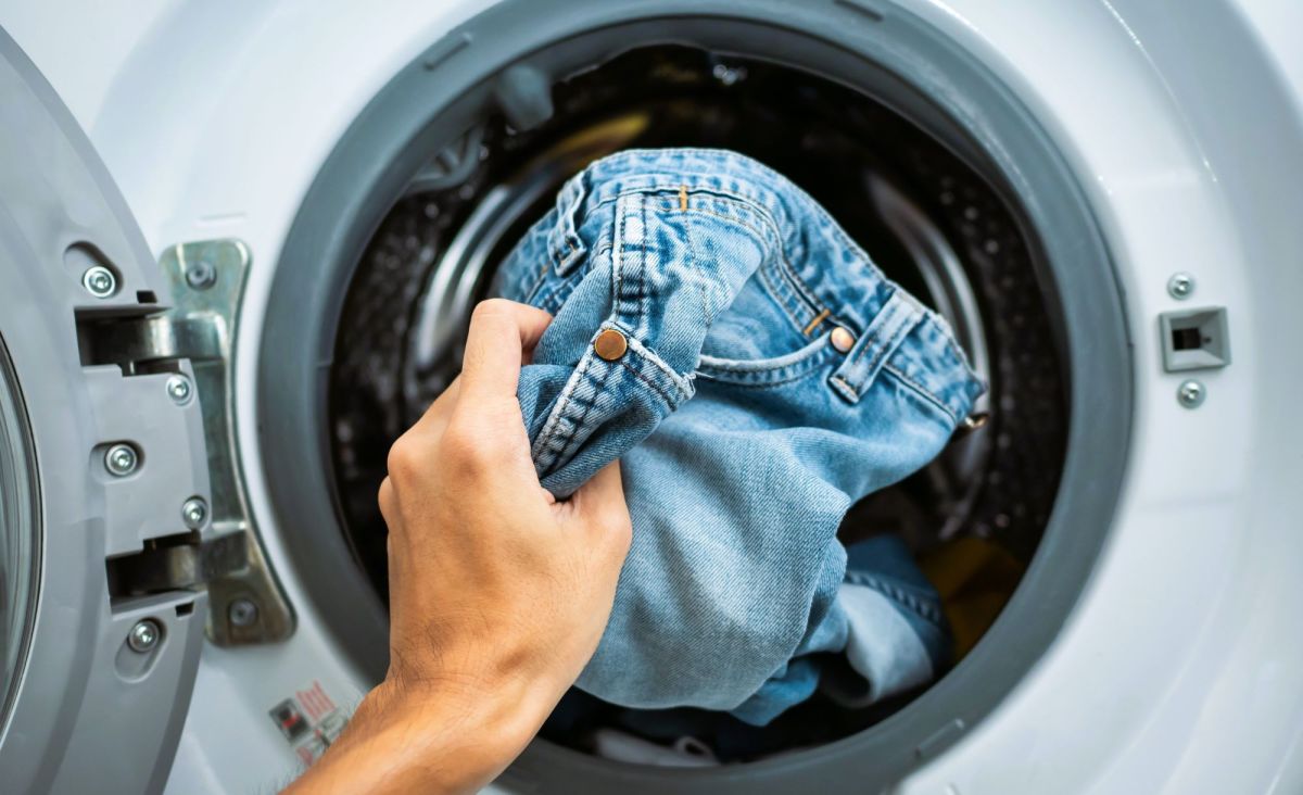 Hand steckt Jeans in Waschmaschine