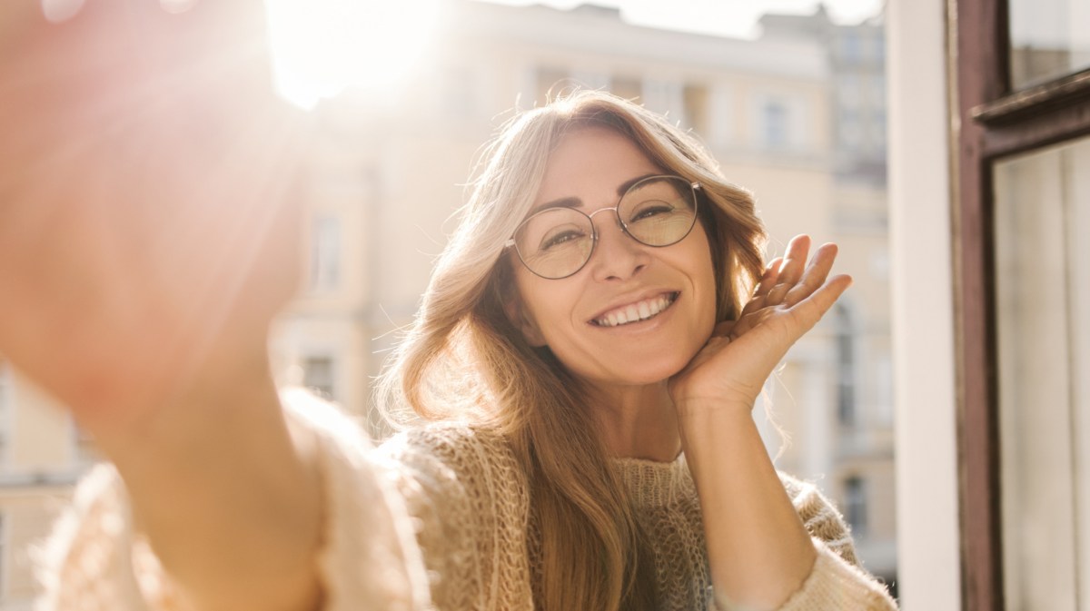 Frau an einem Fenster, die ein Selfie macht und in die Kamera lächelt