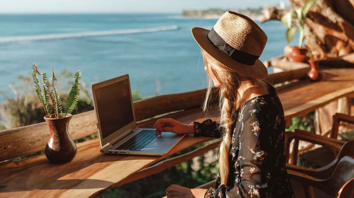 Frau sitzt vor Laptop am Strand.