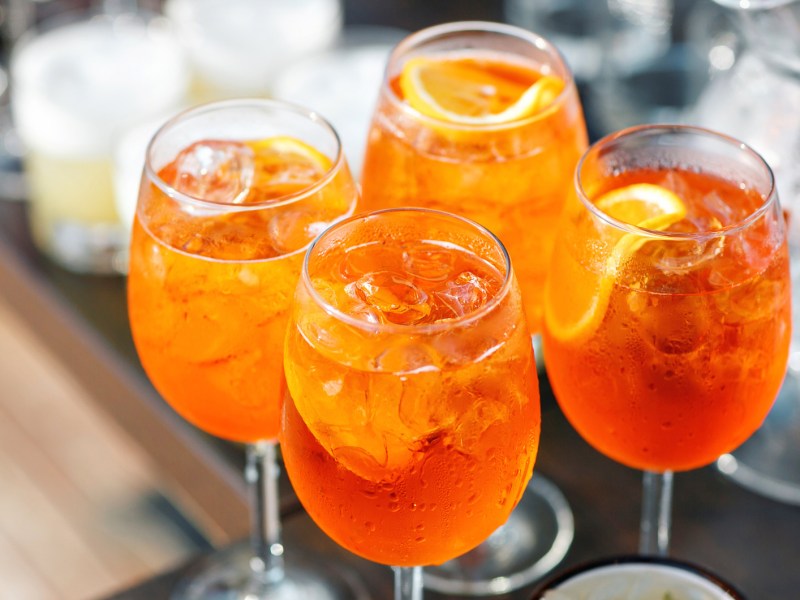 Vier Gläser mit Aperol Spritz auf einem Tisch.