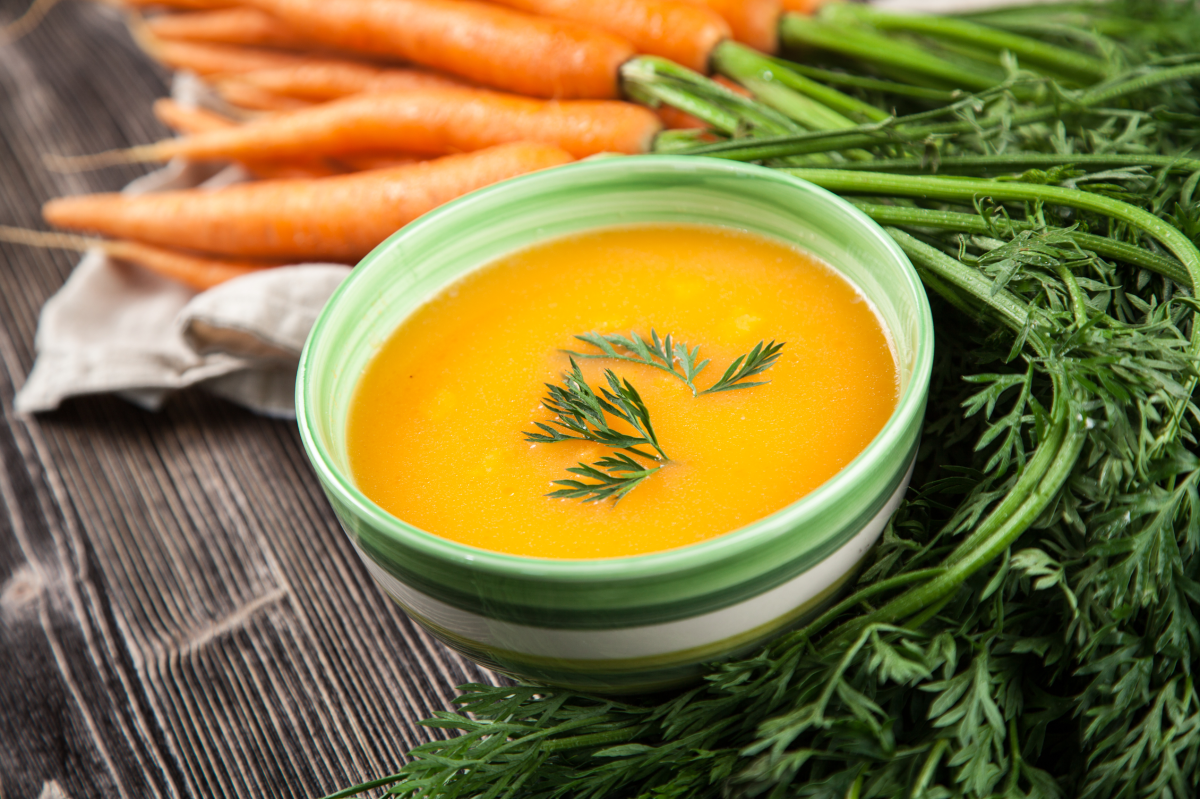 Cremige Karottensuppe in grüner Schale im Hintergrund frische Karotten.