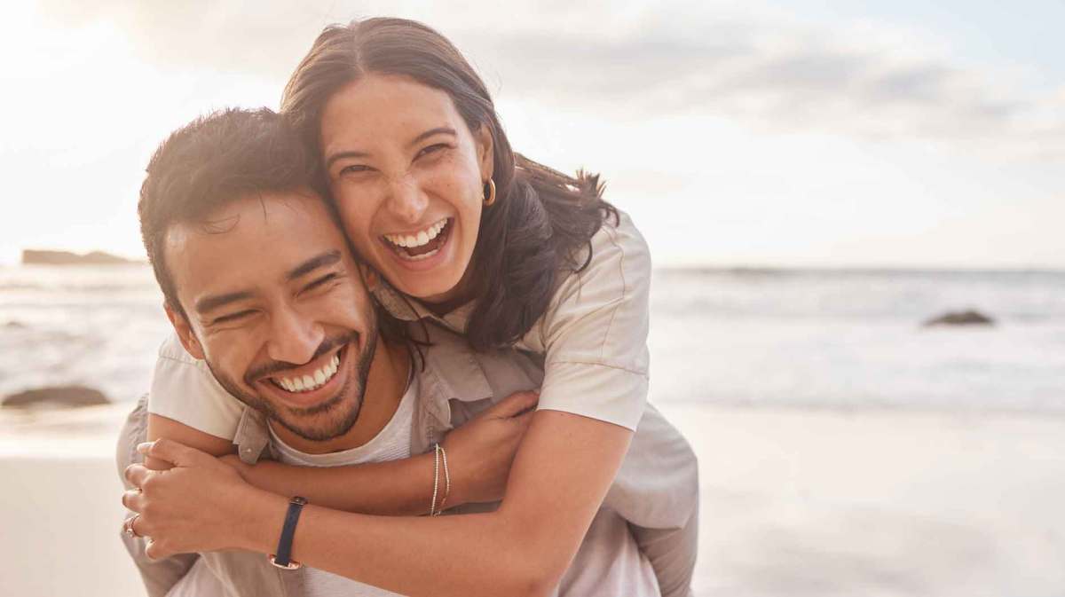 Frau und Mann lachen gemeinsam am Strand.