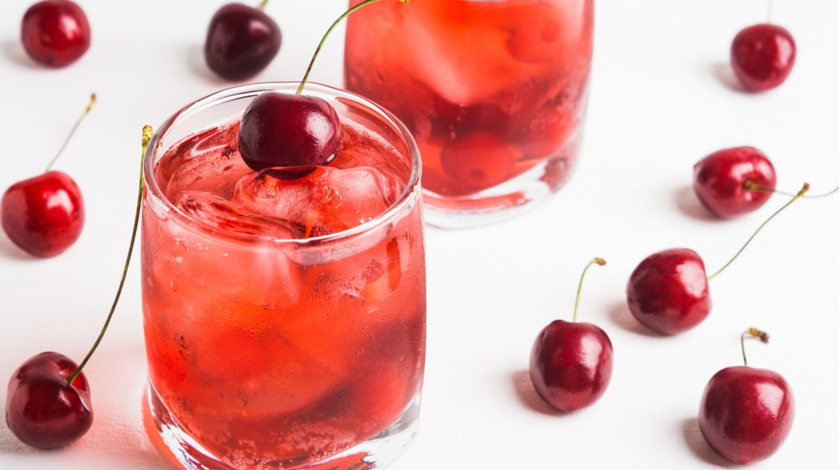 Roter Cocktail mit Eiswürfeln und Kirschen.