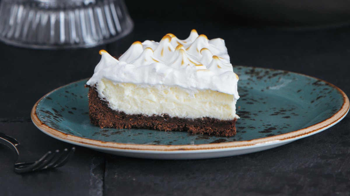 Torte mit dunklem Boden, Puddingschicht und Sahne auf einem blauen Teller.