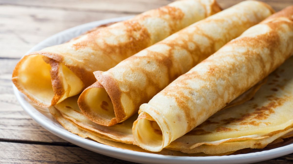 Dünne Crepe-Pfannkuchen auf einem Teller gestapelt, die obersten sind gerollt.